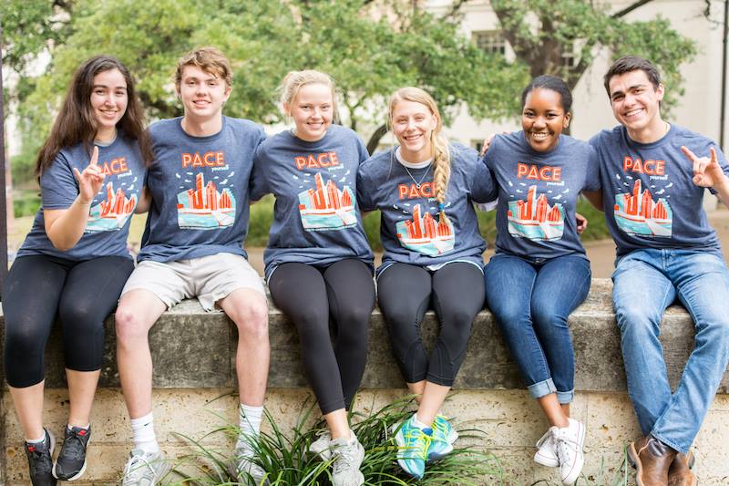 Six students sitting on a wall, wearing PACE t-shirts